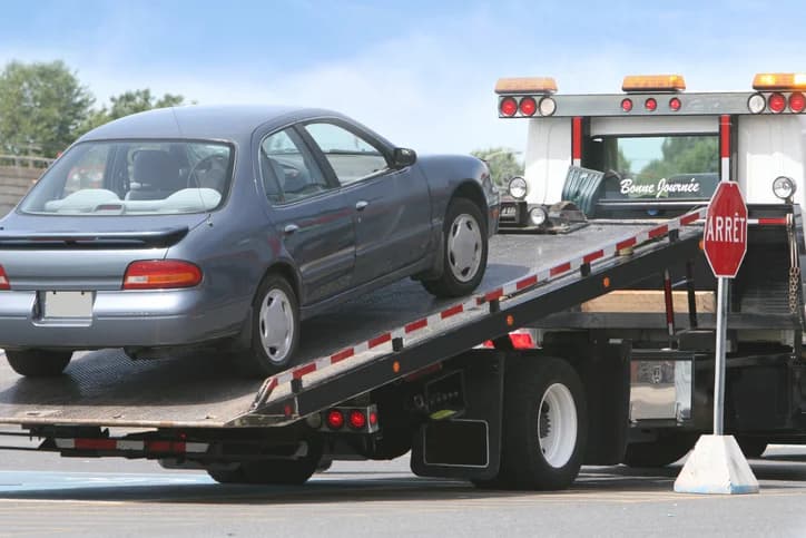Grey sedan being loaded onto a flatbed tow truck for pickup